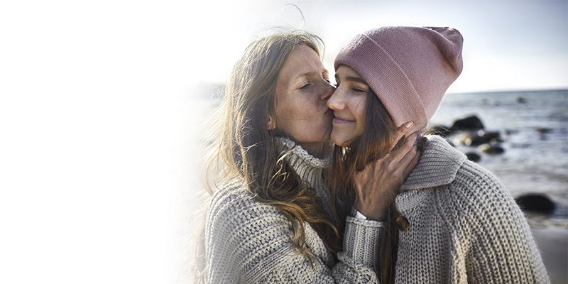 Woman kisses her daughter's cheek on a rocky beach.